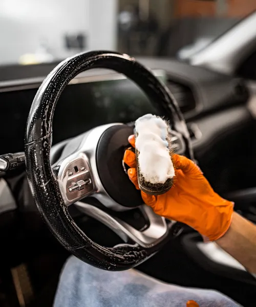 Proces czyszczenia kierownicy we wnętrzu samochodu z użyciem środka czyszczącego.